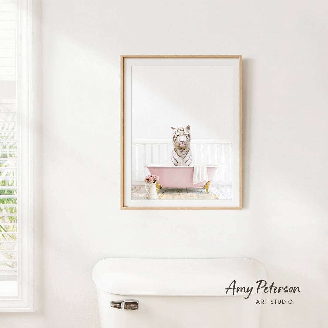 A framed image of a white tiger sitting in a pink bathtub, with a vase of flowers and a white toilet in the foreground.