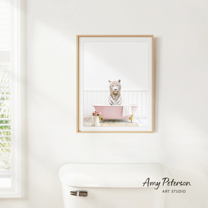 A framed image of a white tiger sitting in a pink bathtub, with a vase of flowers and a white toilet in the foreground.