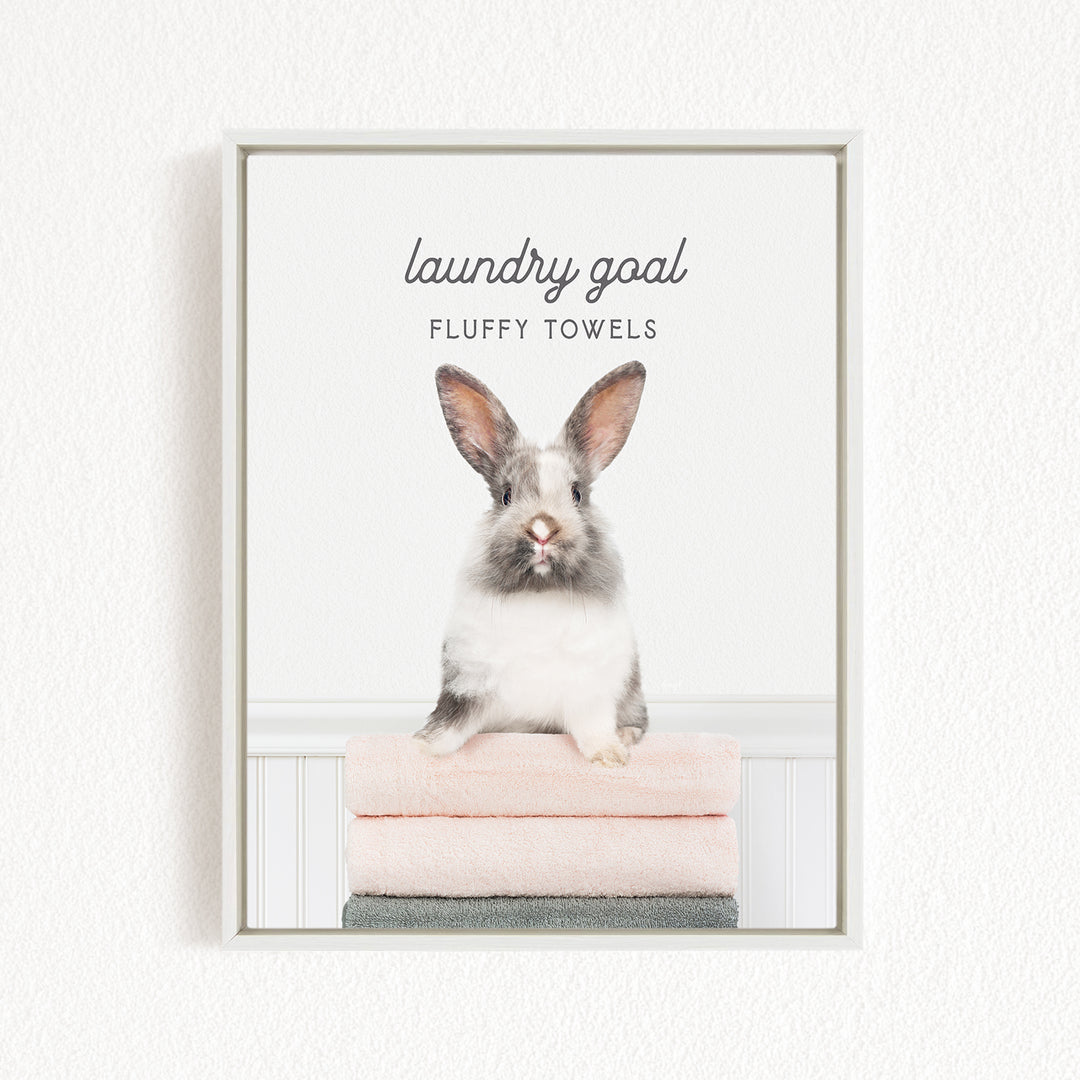 A fluffy white rabbit sitting on a stack of pink towels, with the text "laundry goal" and "fluffy towels" displayed above the image.