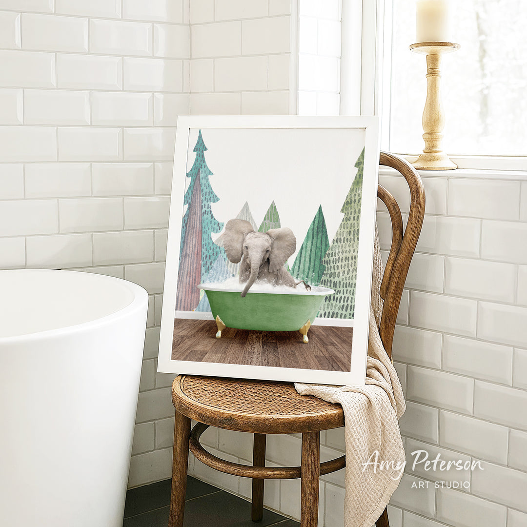 A framed image of an elephant sitting in a green bathtub, surrounded by trees, is displayed on a wooden chair in a bathroom setting.