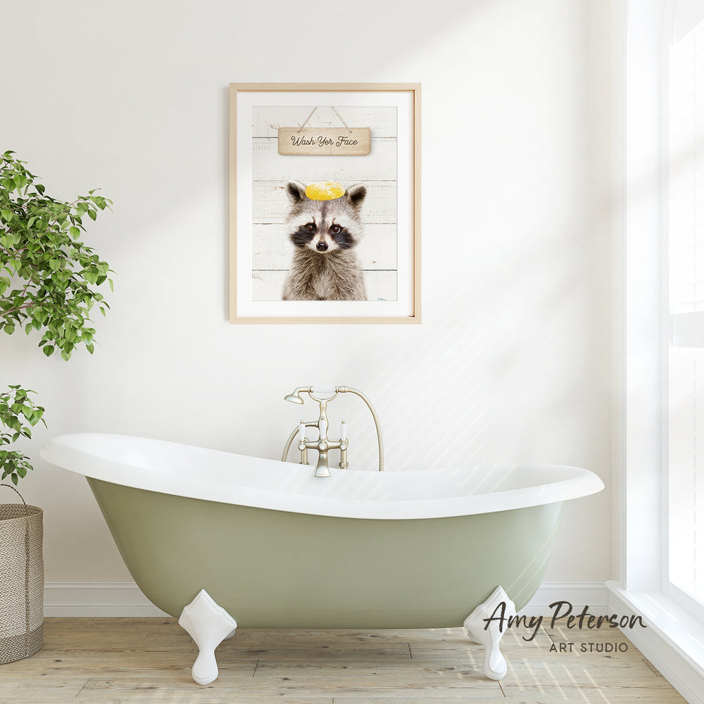 a green clawfoot bathtub with a framed picture of a raccoon above it, hanging on a white wall.