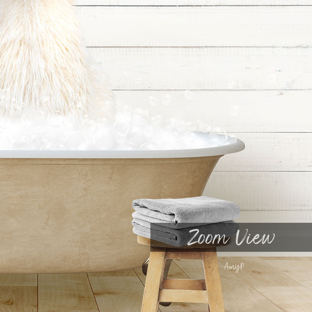 A bathtub filled with bubbles, with a towel and stool in front of it, against a white wooden wall.