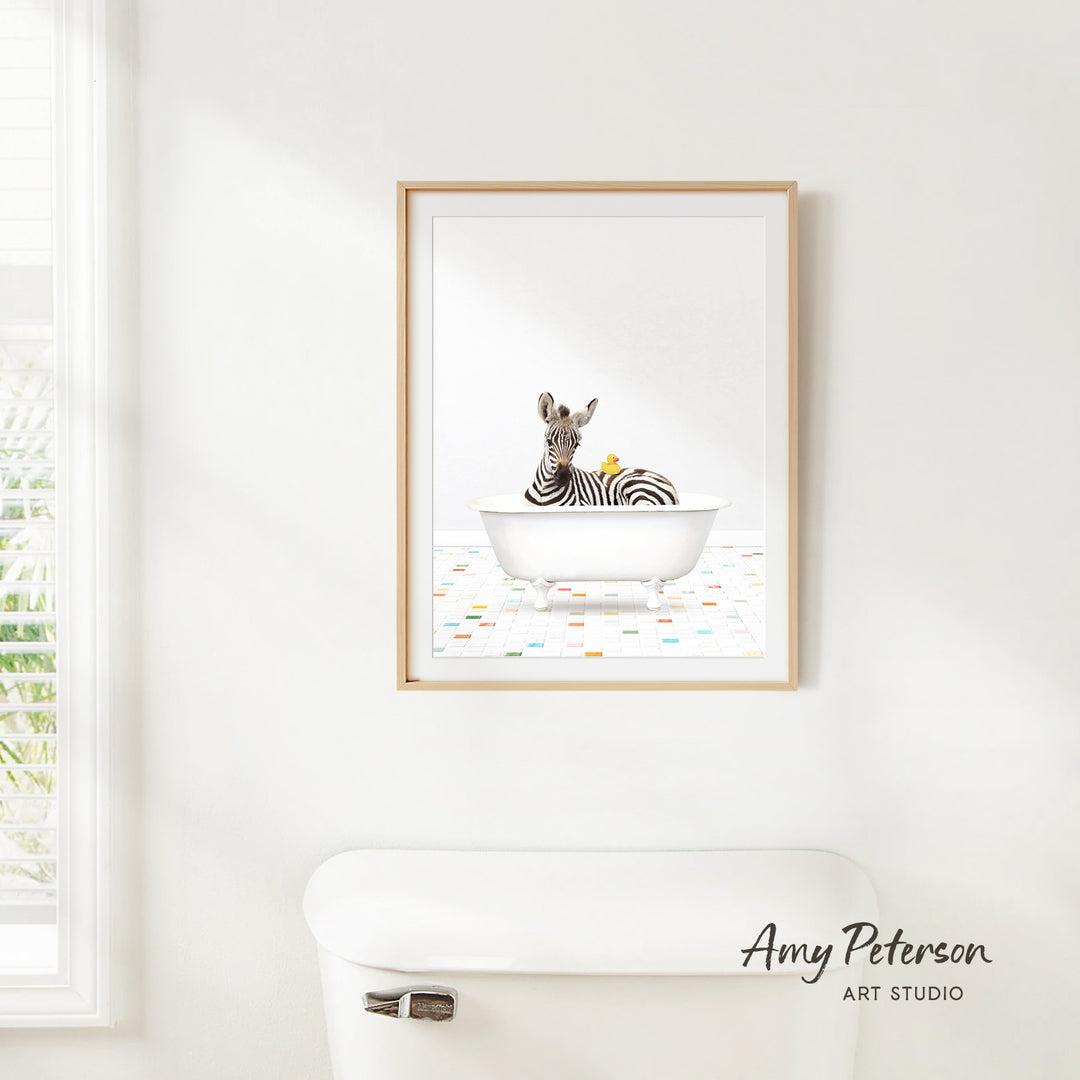 A framed print of a zebra sitting in a bathtub, surrounded by colorful tiles, is hanging on a white wall in a bathroom.