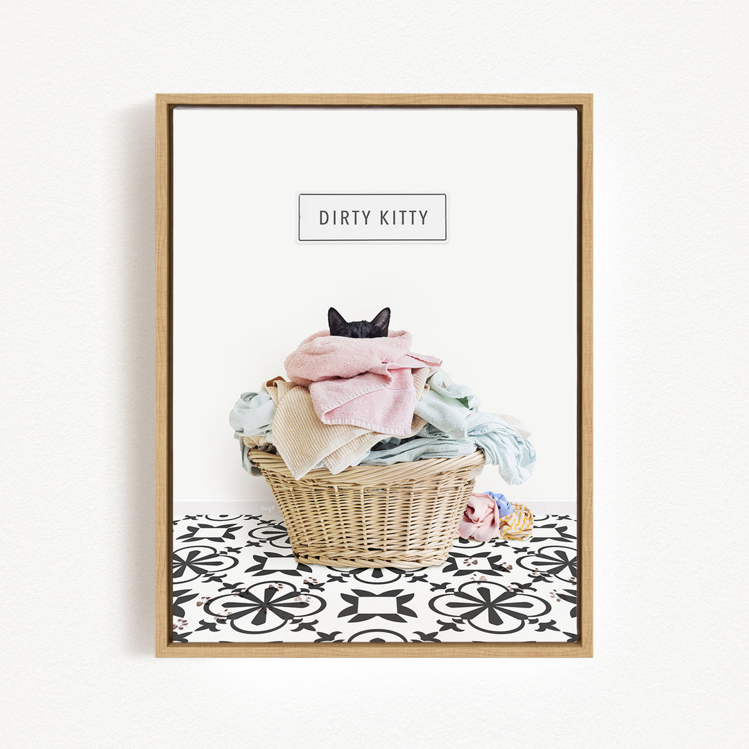 A framed image depicting a cat sitting in a basket filled with clothes, with the text "Dirty Kitty" displayed above the basket.