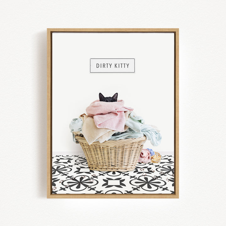 A framed image depicting a cat sitting in a basket filled with clothes, with the text "Dirty Kitty" displayed above the basket.