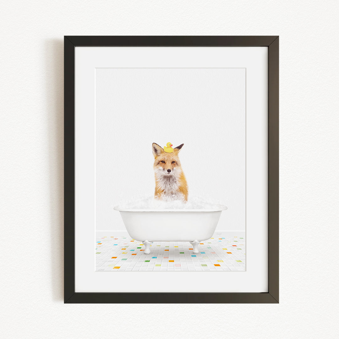 A framed image of a fox sitting in a white bathtub filled with bubbles, with a yellow rubber duck on its head.