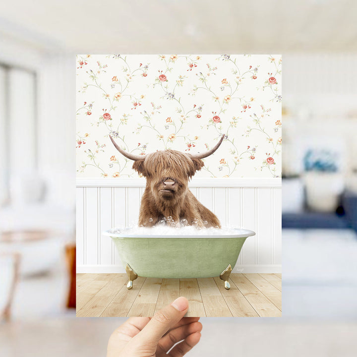 A brown cow with horns is sitting in a green bathtub filled with bubbles, with a floral wallpaper in the background.