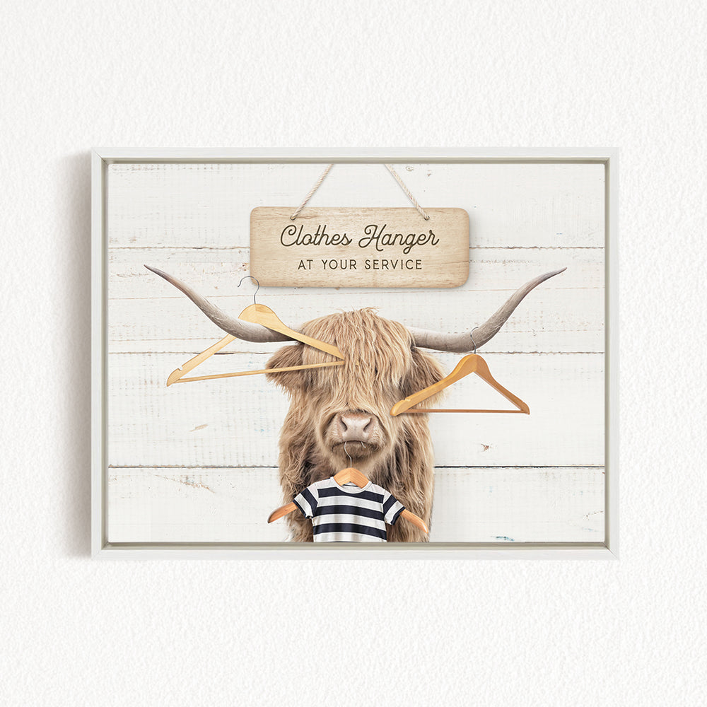 A wooden sign with the text "Clothes Hanger at your service" hangs above a large, furry animal with long horns, which appears to be a yak or a similar animal.