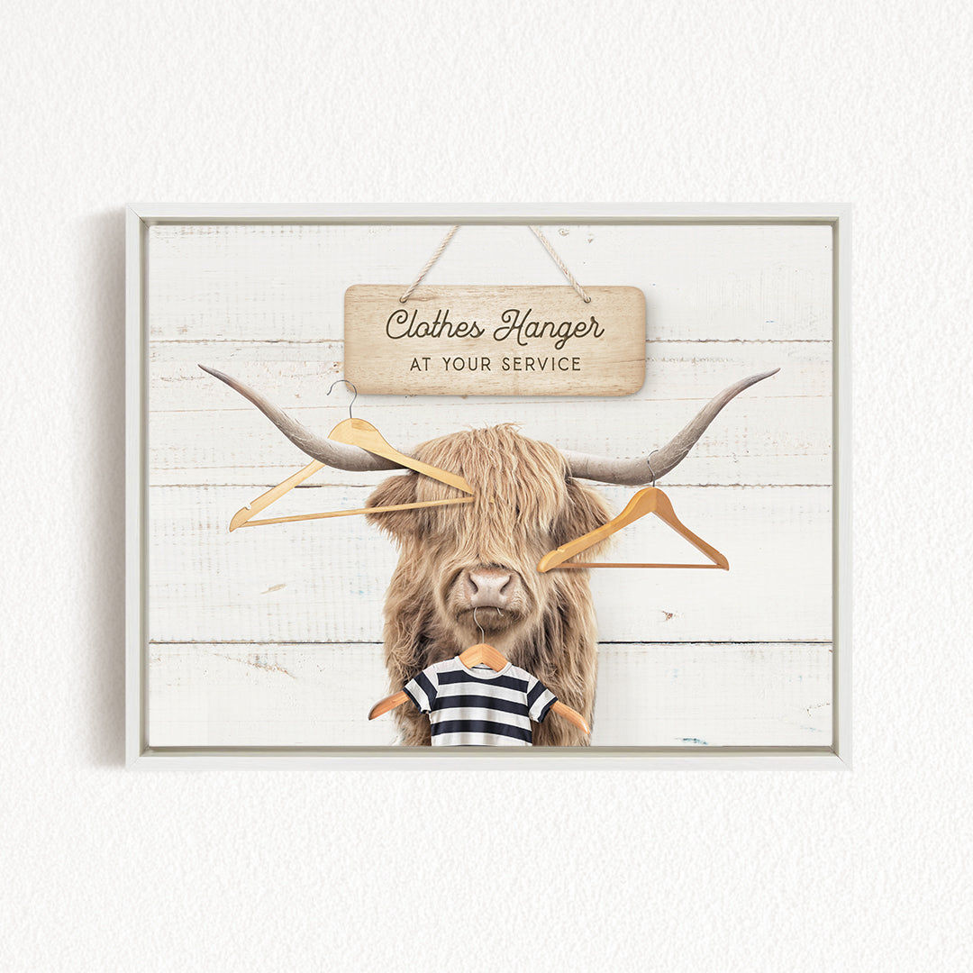A wooden sign with the text "Clothes Hanger at your service" hangs above a large, furry animal with long horns, which appears to be a yak or a similar animal.