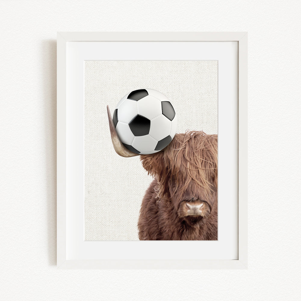 A framed image of a Highland cow balancing a soccer ball on its head.