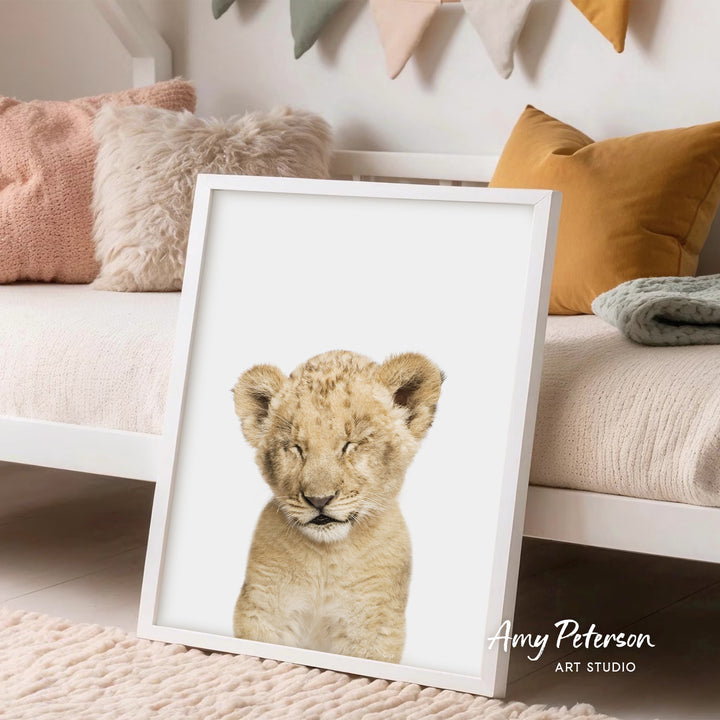 A framed image of a young lion cub is displayed in a cozy bedroom setting with a white bed, colorful pillows, and a rug.