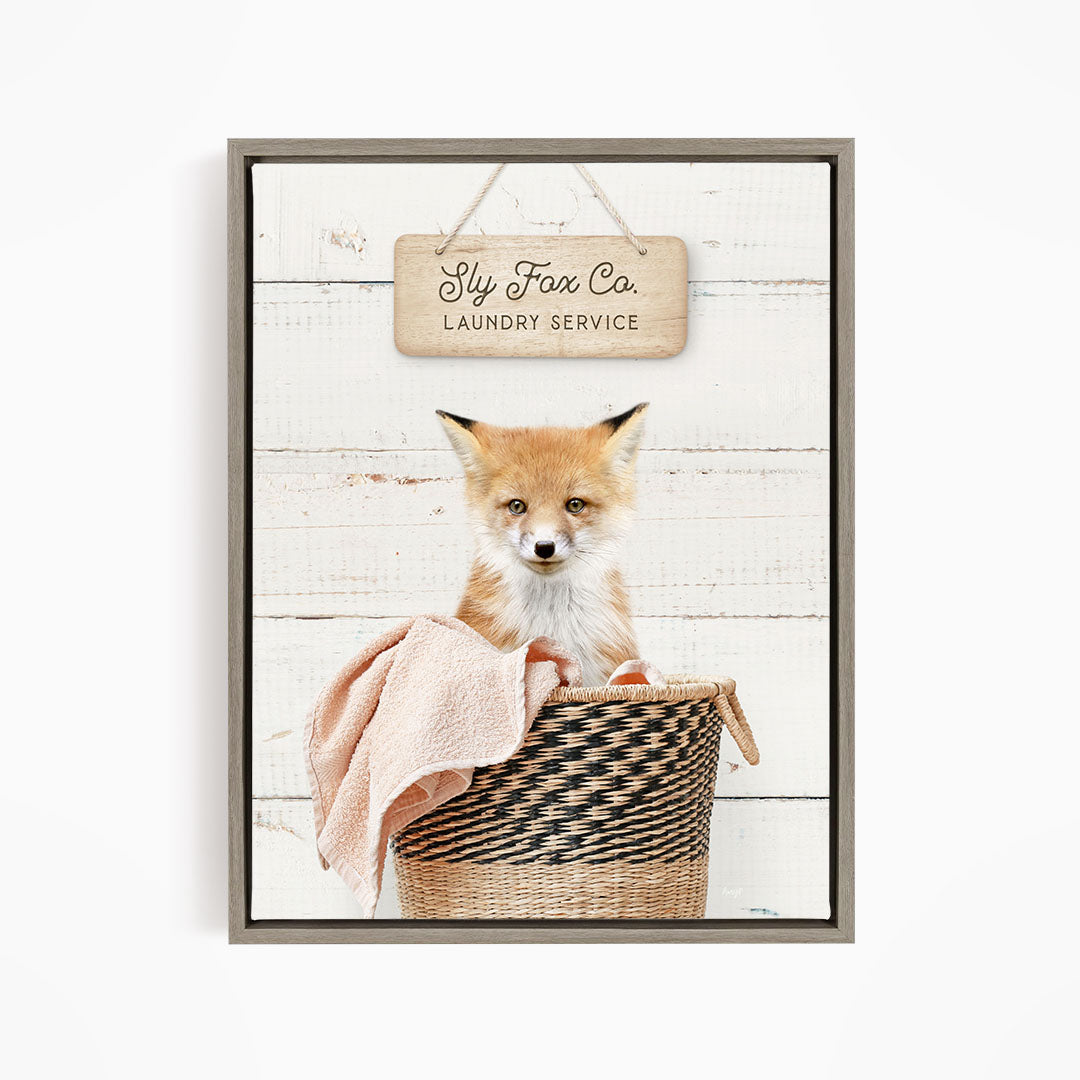 A framed image of a young fox sitting in a woven laundry basket, with a sign above that reads "Laundry Service".