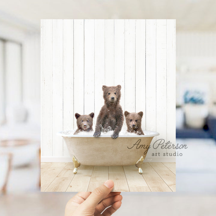 a hand holding a photo of three bears in a bathtub