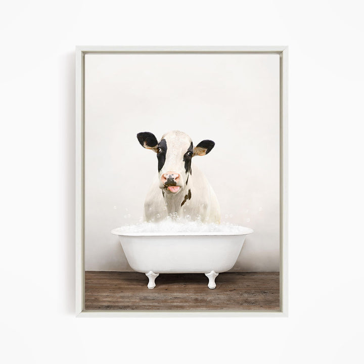 A black and white cow is sitting in a white bathtub filled with water, creating a whimsical and humorous scene.