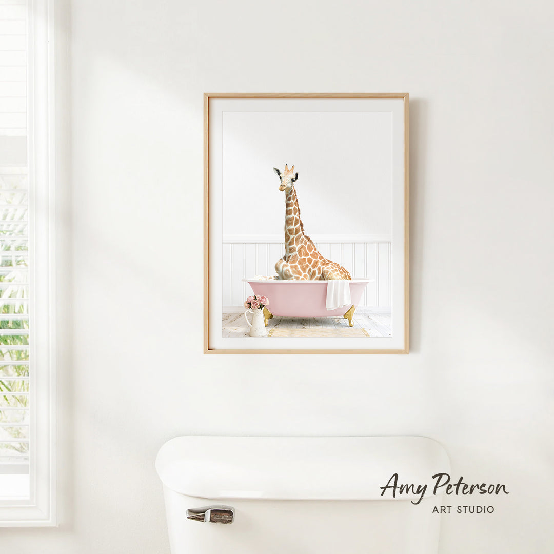 A framed image of a giraffe sitting in a pink bathtub, with a vase of flowers and a white toilet in the foreground.