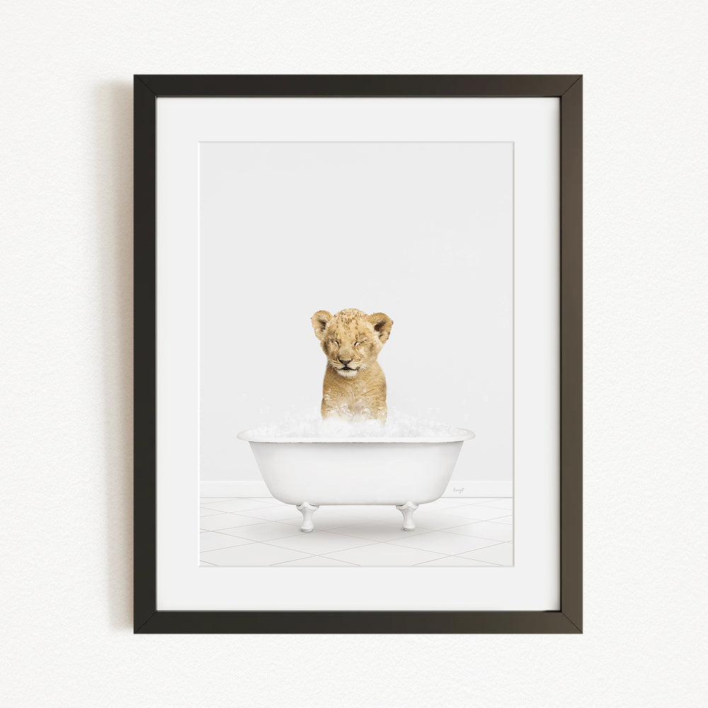 A young lion cub sitting in a white bathtub filled with water, looking directly at the camera.