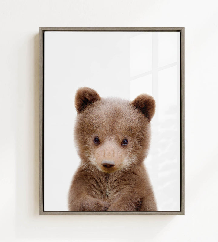 A cute brown bear cub with large eyes and a curious expression is the focus of the framed image.