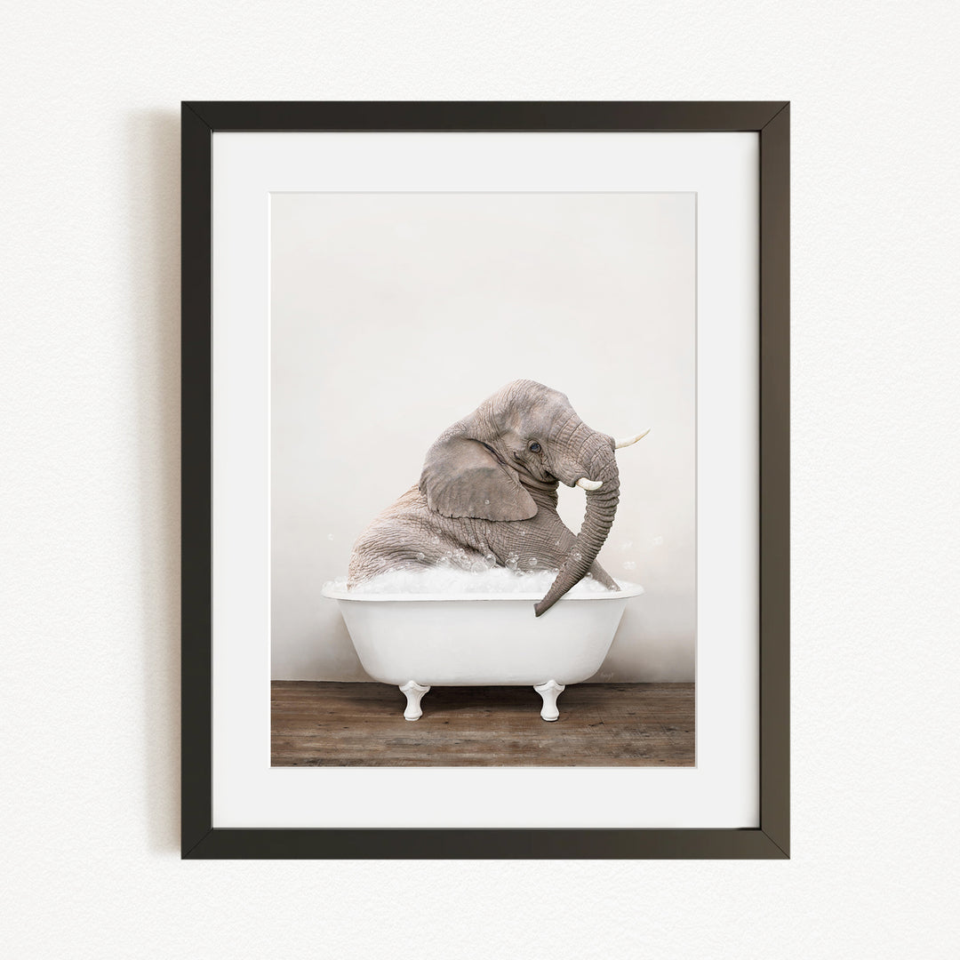 A gray elephant is sitting in a white bathtub, with its trunk raised and appearing to be enjoying a bath.