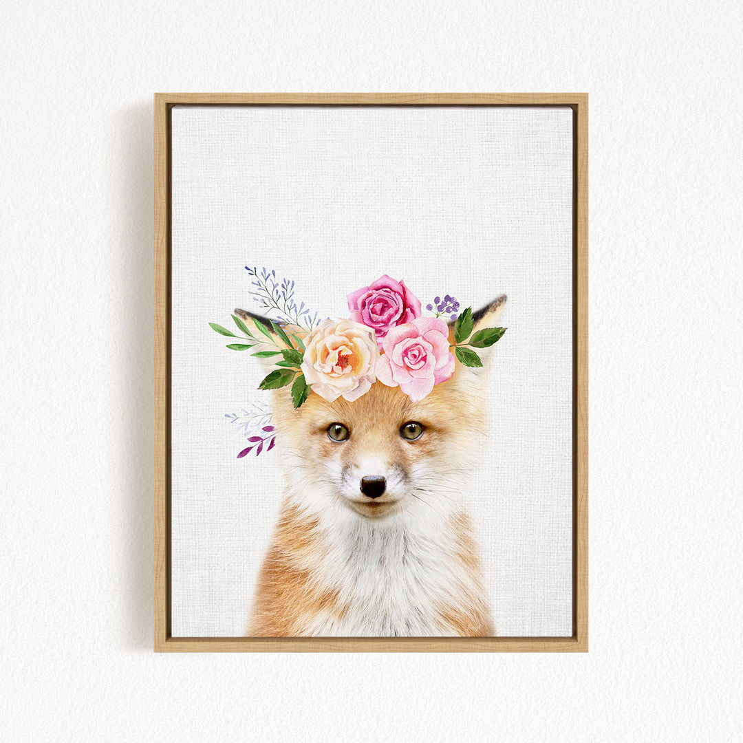 A framed print of a fox wearing a floral crown of pink and white roses and greenery.
