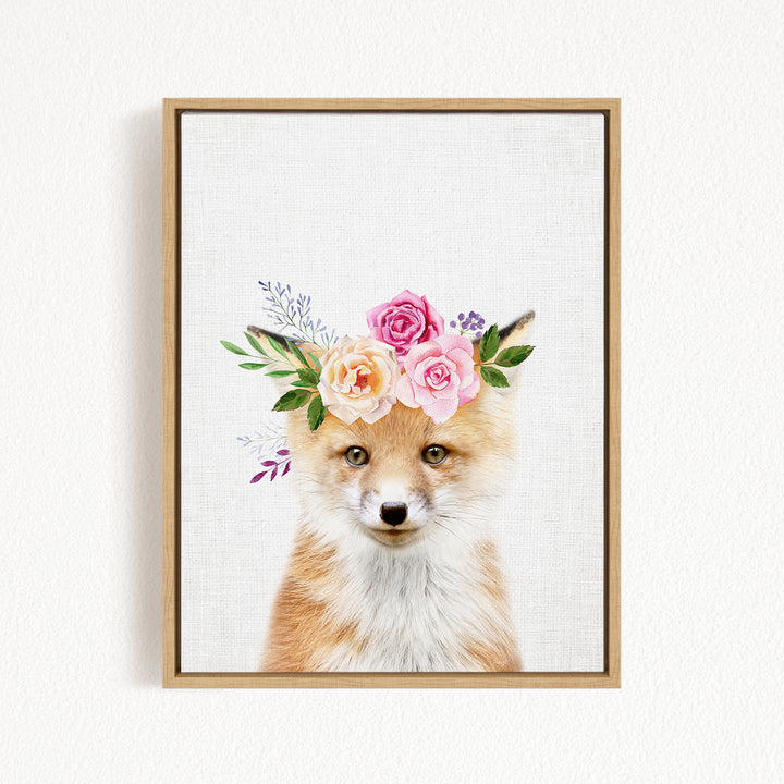 A framed print of a fox wearing a floral crown of pink and white roses and greenery.