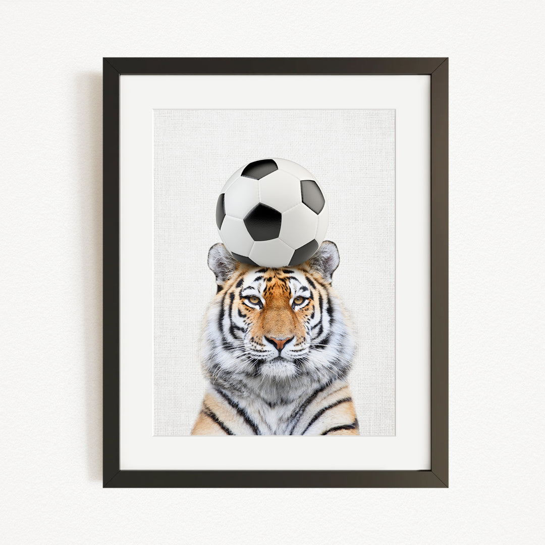 A tiger is sitting on a soccer ball, with the ball balanced on its head.