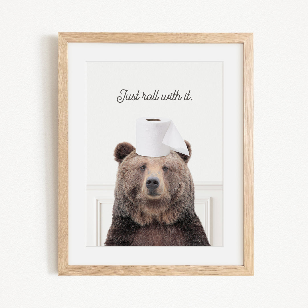 A framed image of a brown bear wearing a roll of toilet paper on its head, with the text "Just roll with it."