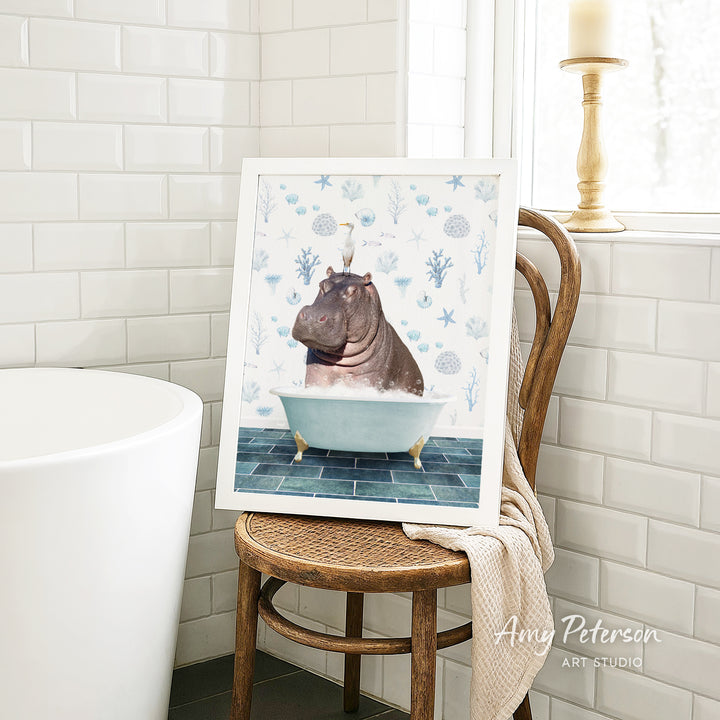 A framed image of a hippopotamus sitting in a bathtub is displayed on a wooden chair in a bathroom setting.