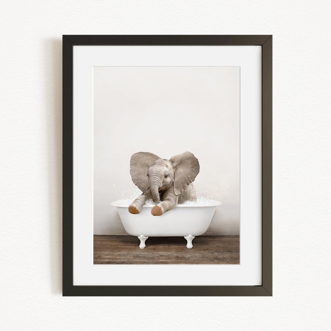 A baby elephant sitting in a white bathtub, with its trunk raised and ears spread out.