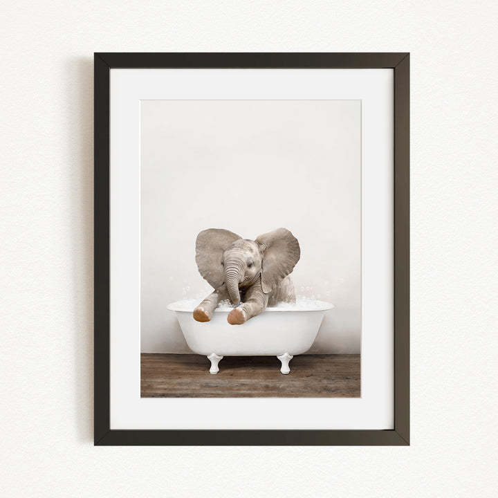 A baby elephant sitting in a white bathtub, with its trunk raised and ears spread out.