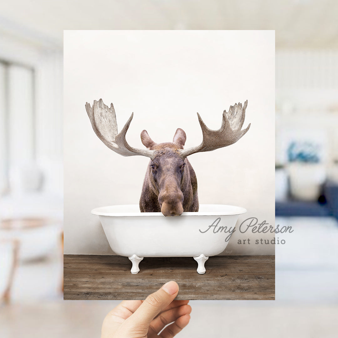 a hand holding up a photo of a moose in a bathtub