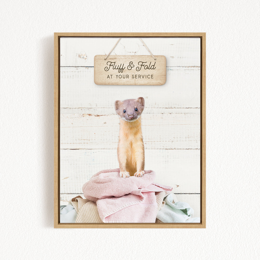 A cute beige cat sitting on a pink blanket, with a wooden sign above that says "Fluffy & Fold at your Service".