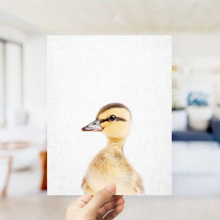 A hand is holding up a white square with a close-up of a duck's face on it.