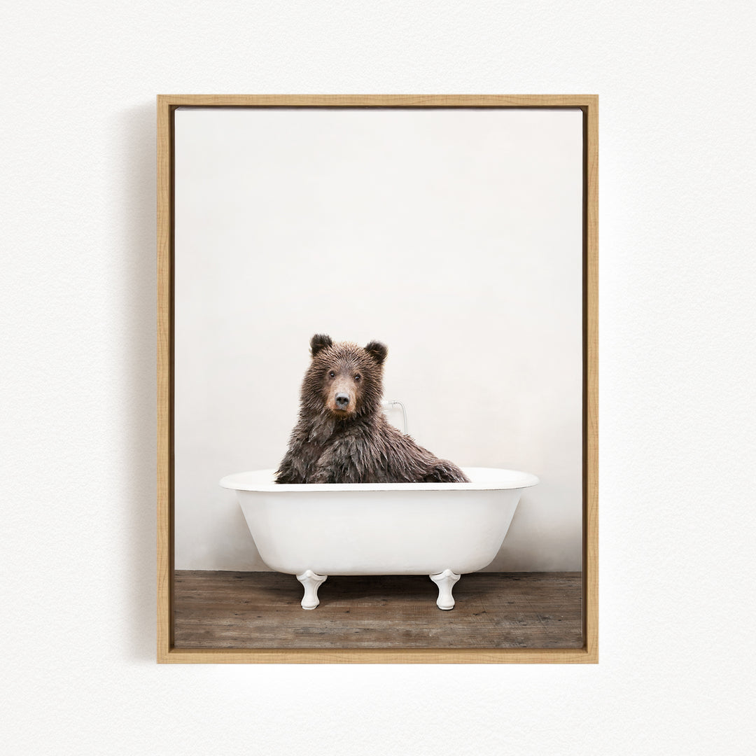 A brown bear sitting in a white bathtub against a plain white wall.
