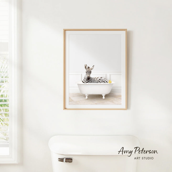 A framed image of a zebra sitting in a white bathtub, with a yellow rubber duck floating on the water.
