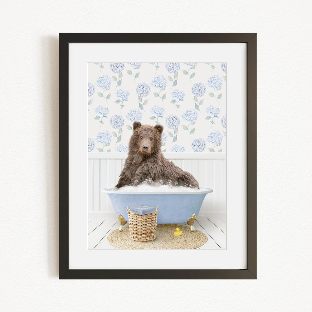 A brown bear is sitting in a blue bathtub filled with bubbles, surrounded by a floral patterned wall and a basket of rubber ducks.