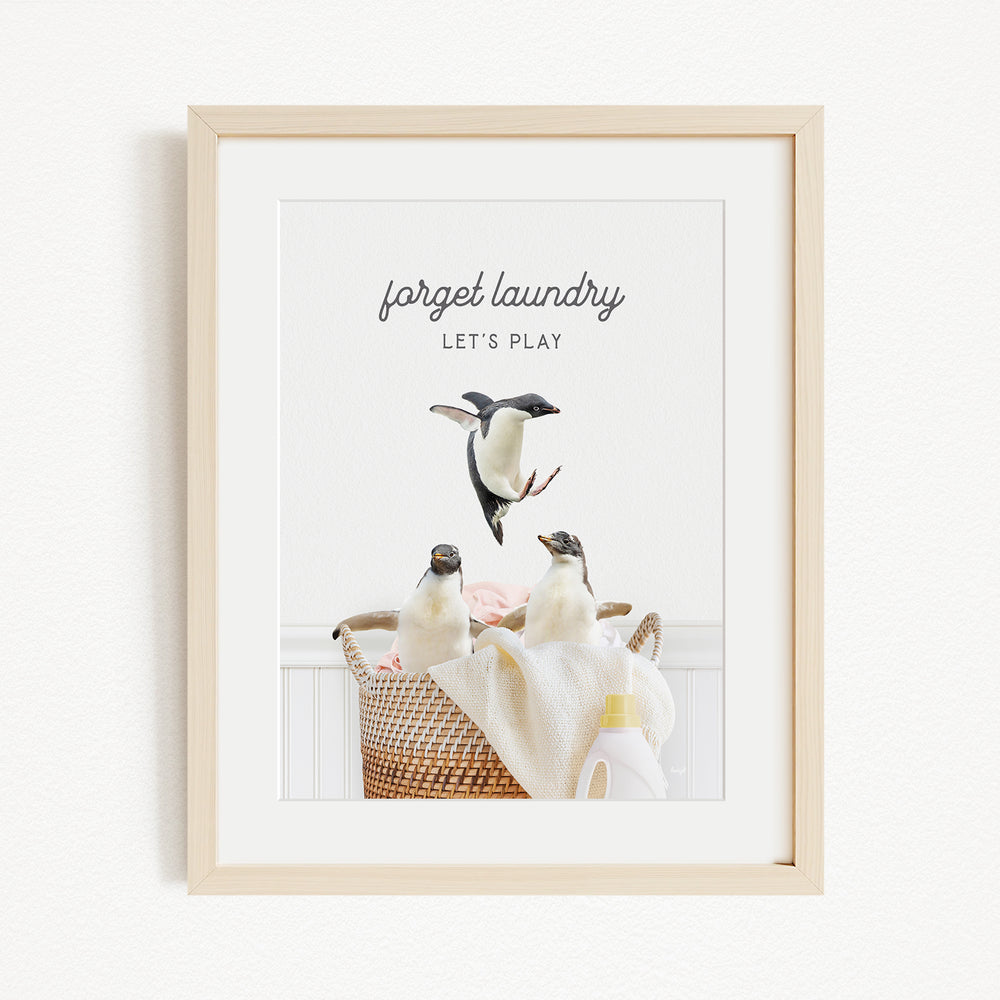 A framed image of three penguins in a basket, with the text "Forget laundry, let's play" written above them.