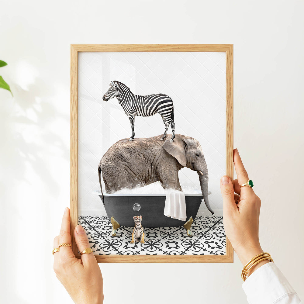 A person's hands are holding a framed image depicting a zebra standing on an elephant's back while the elephant is submerged in a bathtub.
