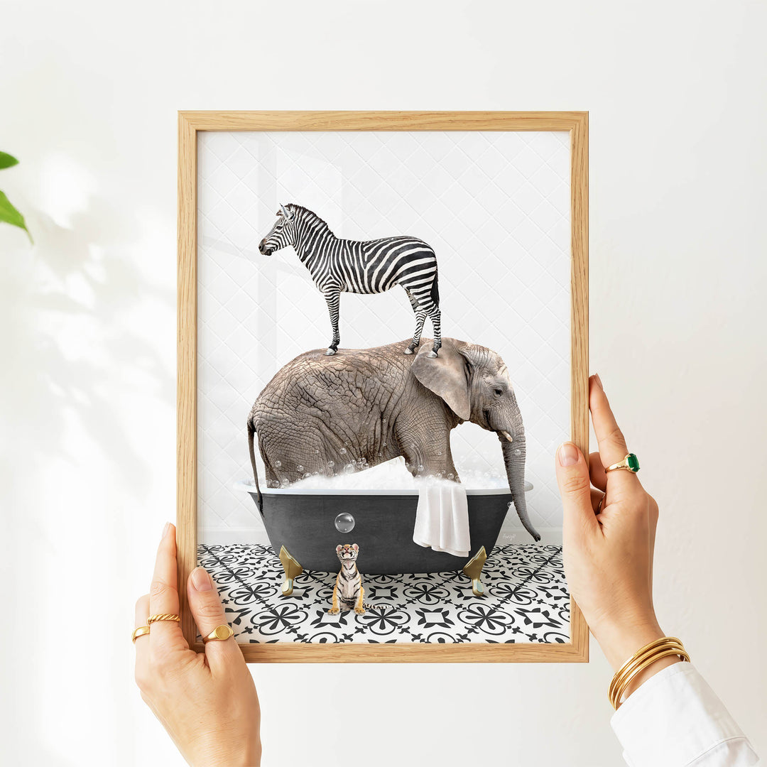 A person's hands are holding a framed image depicting a zebra standing on an elephant's back while the elephant is submerged in a bathtub.