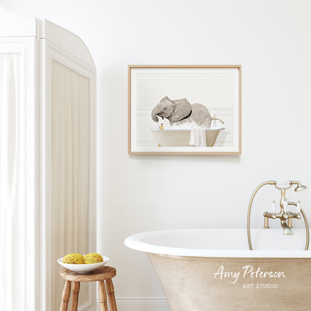 a bathroom scene with a framed picture of an elephant sitting in a bathtub, a wooden stool with a bowl of fruit, and a faucet.
