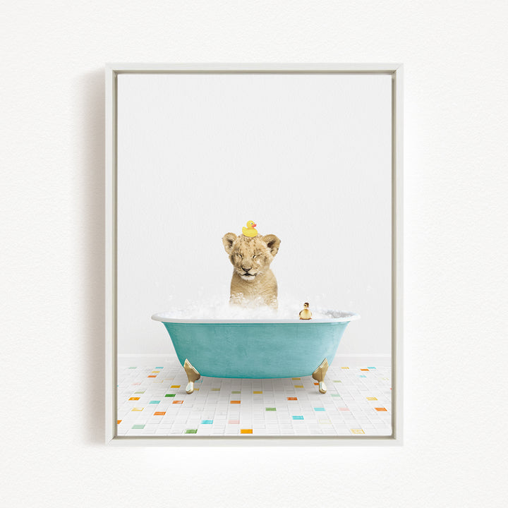 A young lion cub is sitting in a blue bathtub filled with bubbles, with two yellow rubber ducks floating on its head.