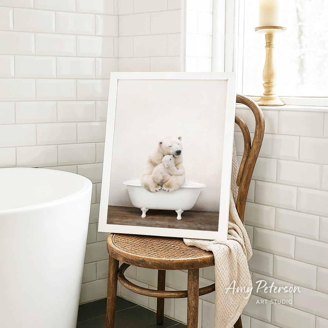A framed photograph of two polar bears sitting in a bathtub is displayed on a wooden chair in a bathroom setting.