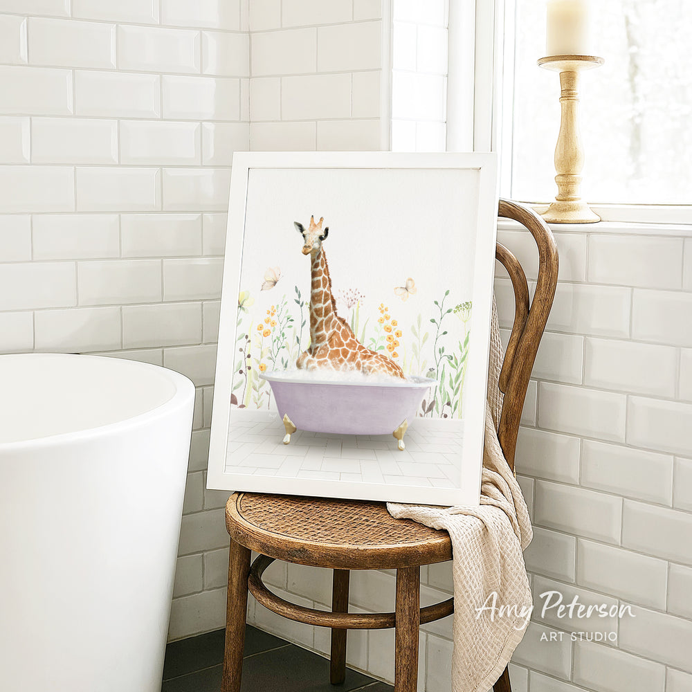 A framed illustration of a giraffe sitting in a bathtub, surrounded by flowers and butterflies, is displayed on a wooden chair in a bathroom setting.