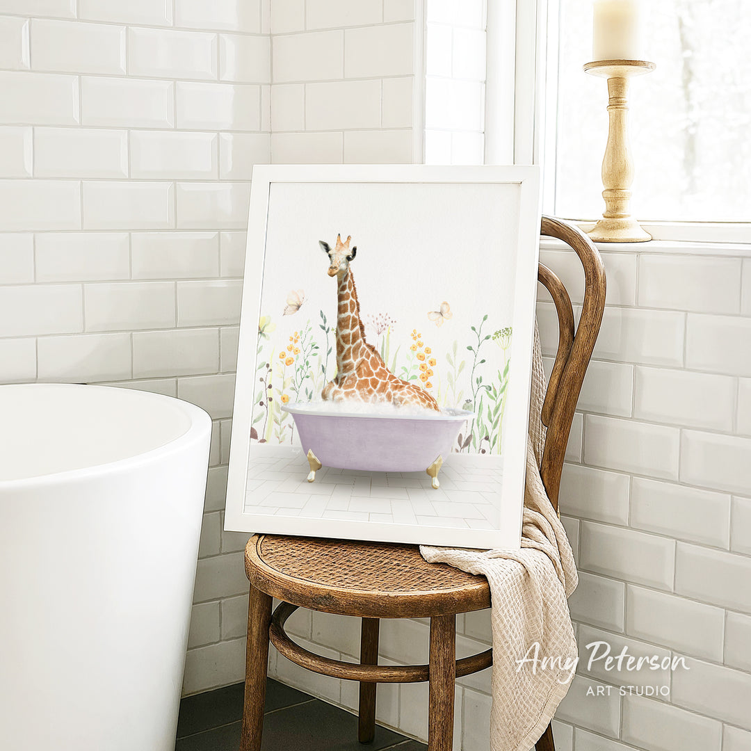 A framed illustration of a giraffe sitting in a bathtub, surrounded by flowers and butterflies, is displayed on a wooden chair in a bathroom setting.