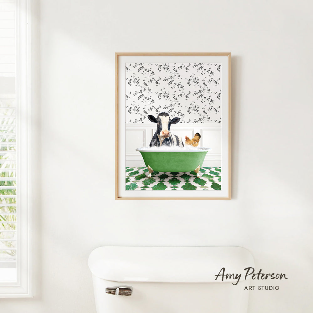 A framed image of a cow sitting in a green bathtub, with a chicken in the tub, is hanging on a white wall.