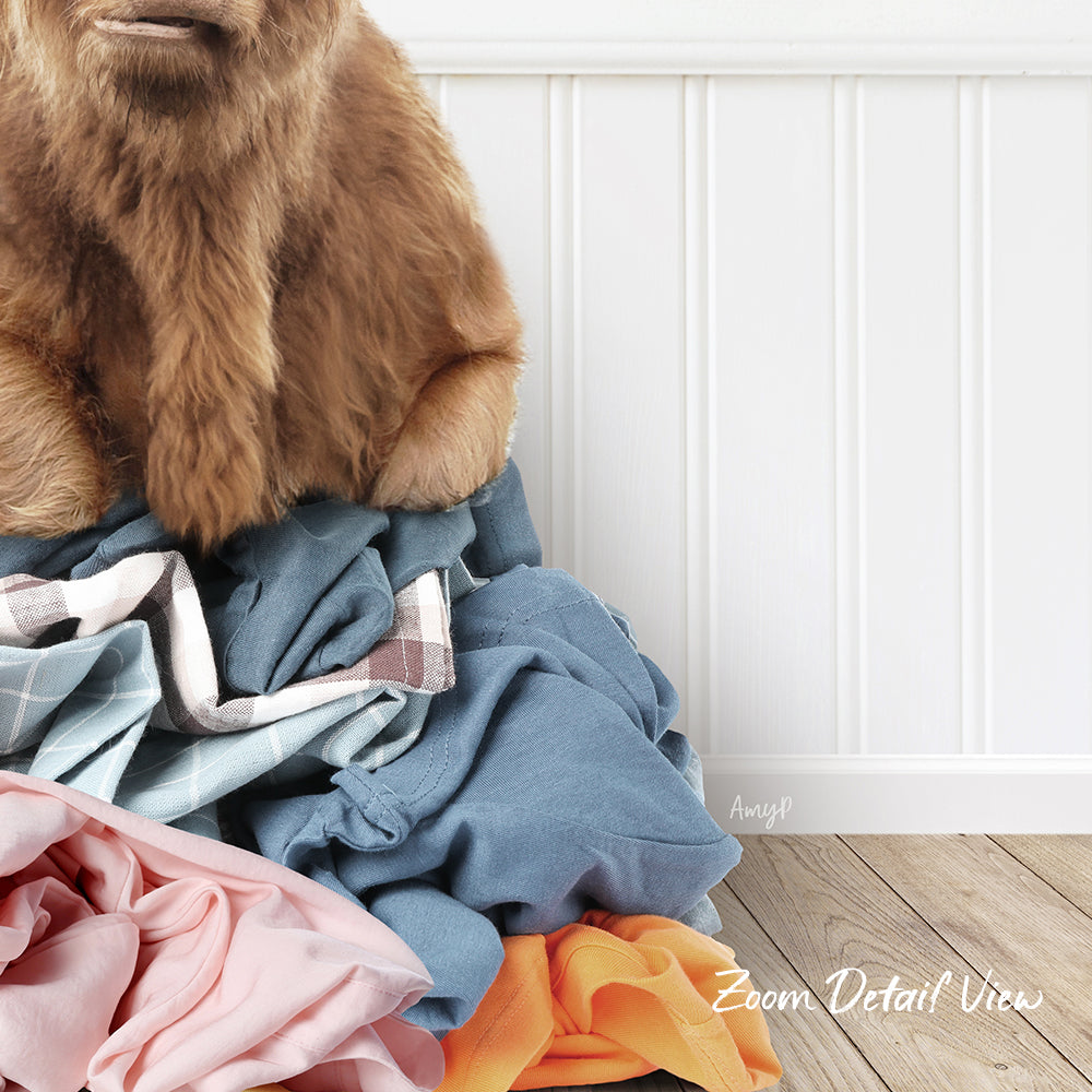 A close-up of a dog's head peeking over a pile of clothes, with a white wall and wooden floor in the background.