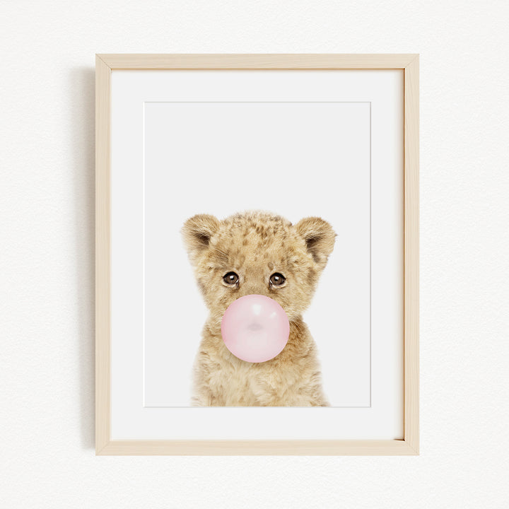 A cute baby lion blowing a bubble with a pink bubble gum bubble.