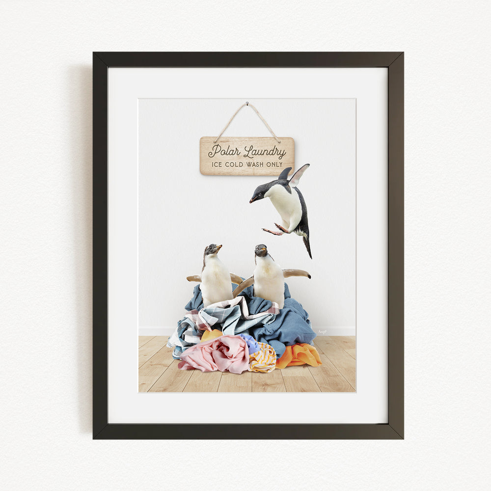 A framed photograph of two penguins sitting on a pile of clothes, with a sign above them that reads "Polar Laundry Ice Cold Washing".