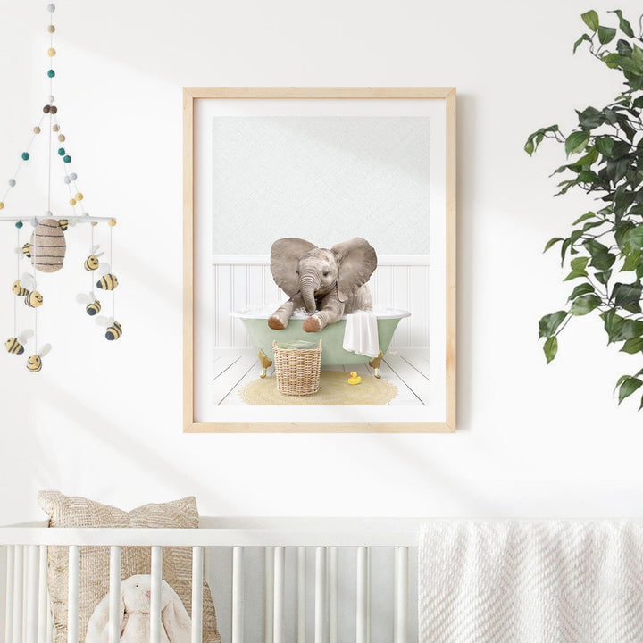 A framed image of a baby elephant sitting in a bathtub, surrounded by various baby toys and a hanging mobile.