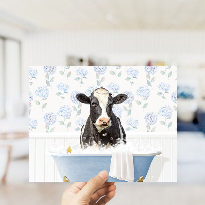 A black and white cow is sitting in a blue bathtub filled with bubbles, with a yellow bird perched on the edge of the tub.