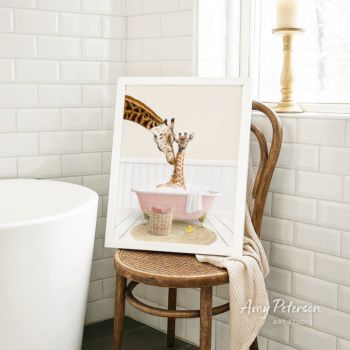A framed image of two giraffes sitting in a pink bathtub, with one giraffe appearing to be bathing the other. The image is displayed on a wooden chair in a bathroom setting.